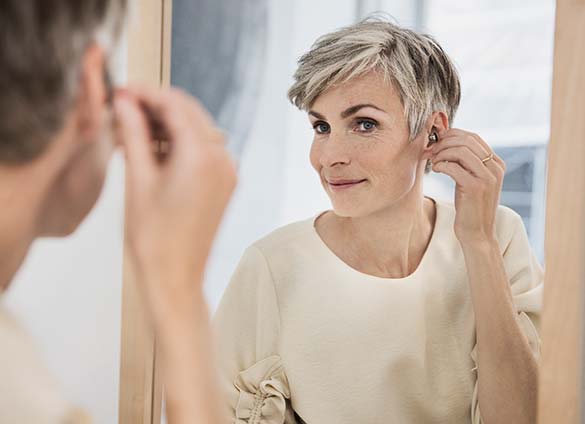 Frau probiert Ihre neuen Hörgeräte vorm Spiegel